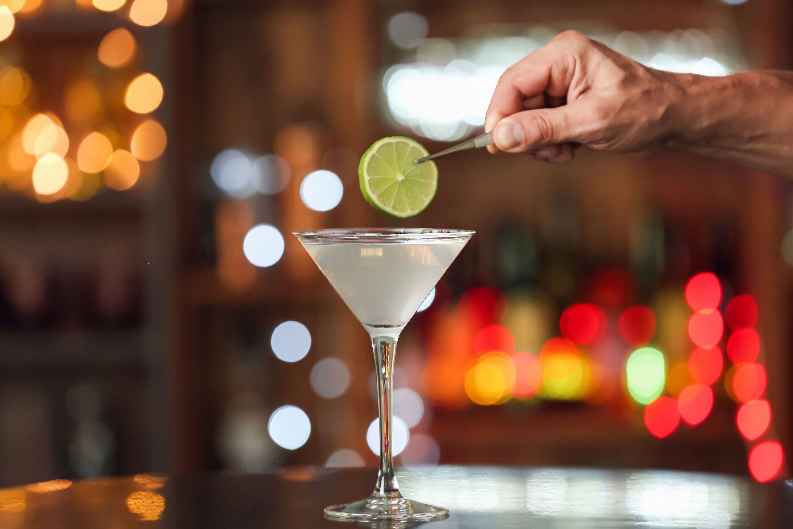 Una mano sosteniendo un gajo de lima sobre una copa de martini.