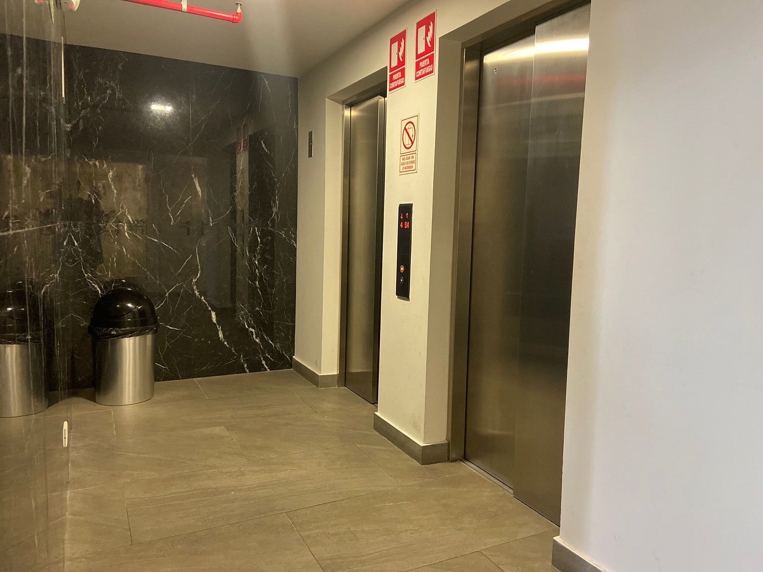 A modern elevator area with marble walls, a trash bin, and a fire extinguisher.
