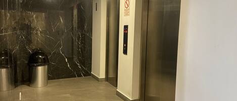 A modern elevator area with marble walls, a trash bin, and a fire extinguisher.