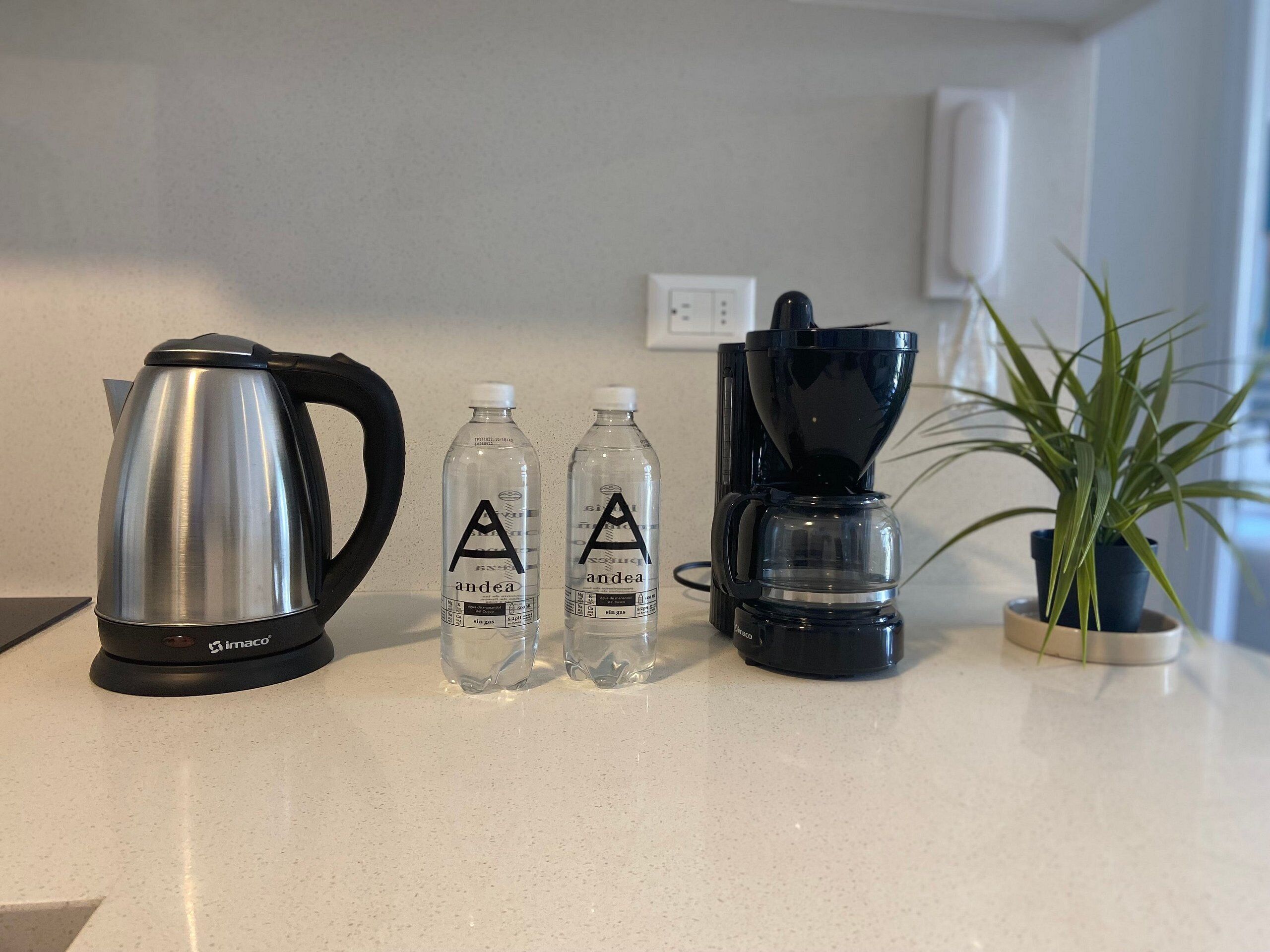 Un piano di lavoro della cucina con una macchina da caffè in acciaio inossidabile, due bottiglie d'acqua e un macinino per caffè nero.