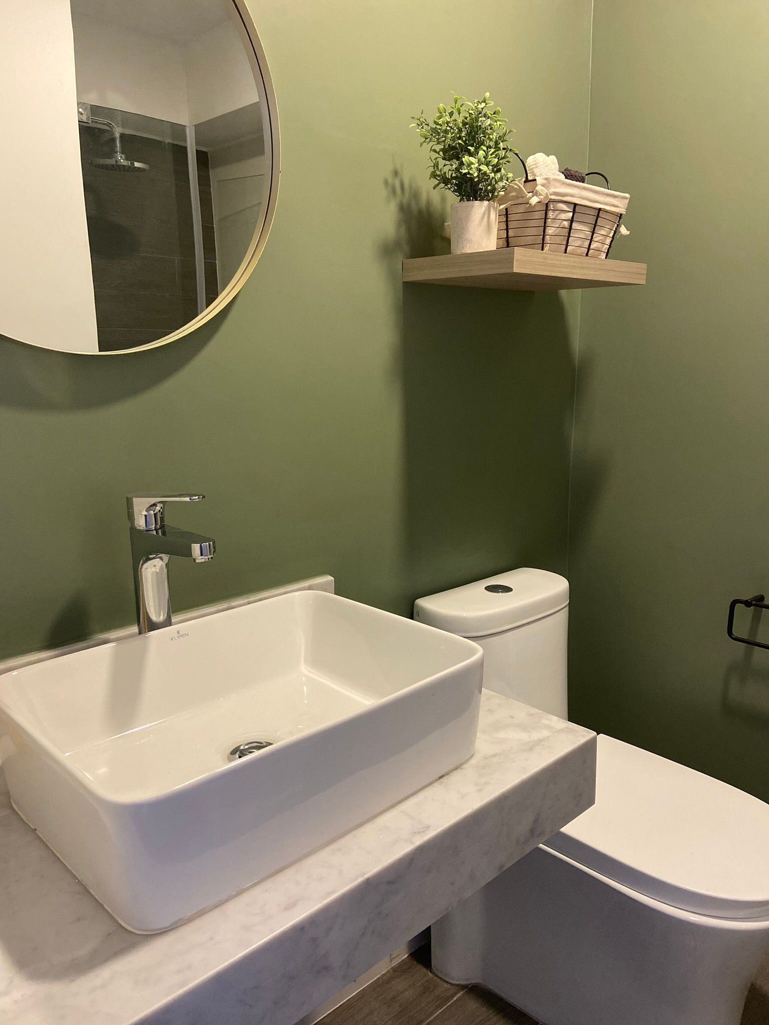A bathroom with a white sink, a toilet, a mirror, and a shelf with a plant and a basket.