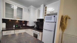A compact kitchen with white cabinets, a dark countertop, a Brandt refrigerator, and a small sink. - Quietstay 20' Paris, Connected Home Avec Terrasse (Massy)
