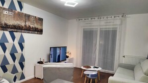 A living room with a flat-screen TV, a small table with a vase, and a couch. - Quietstay 20' Paris, Connected Home Avec Terrasse (Massy)