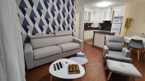 A modern living room with a grey sofa, a small round table with remotes and a board game, and a patterned wall. - Quietstay 20' Paris, Connected Home Avec Terrasse (Massy)