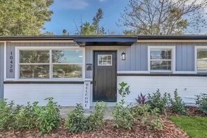 A single-story house with a dark front door, a welcome sign, and a mailbox.