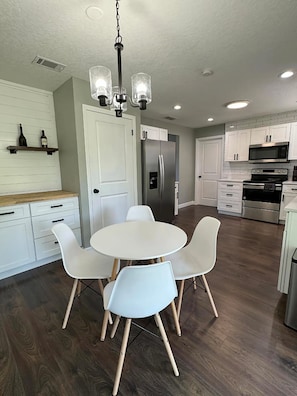 A modern kitchen with white cabinetry, a stainless steel refrigerator, a microwave, and a dining area with a round table and four chairs.