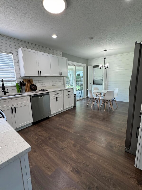 A modern kitchen with white cabinets, a dishwasher, and a dining area with a table and chairs.