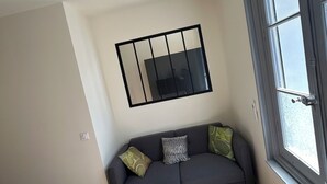 A living room with a grey sofa, a coffee table, and a large window. - Appartement Centre Ville (Castelnaudary)