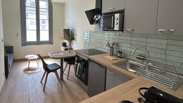 A modern kitchen with grey cabinets, a black microwave, and a wooden countertop. - Appartement Centre Ville (Castelnaudary)