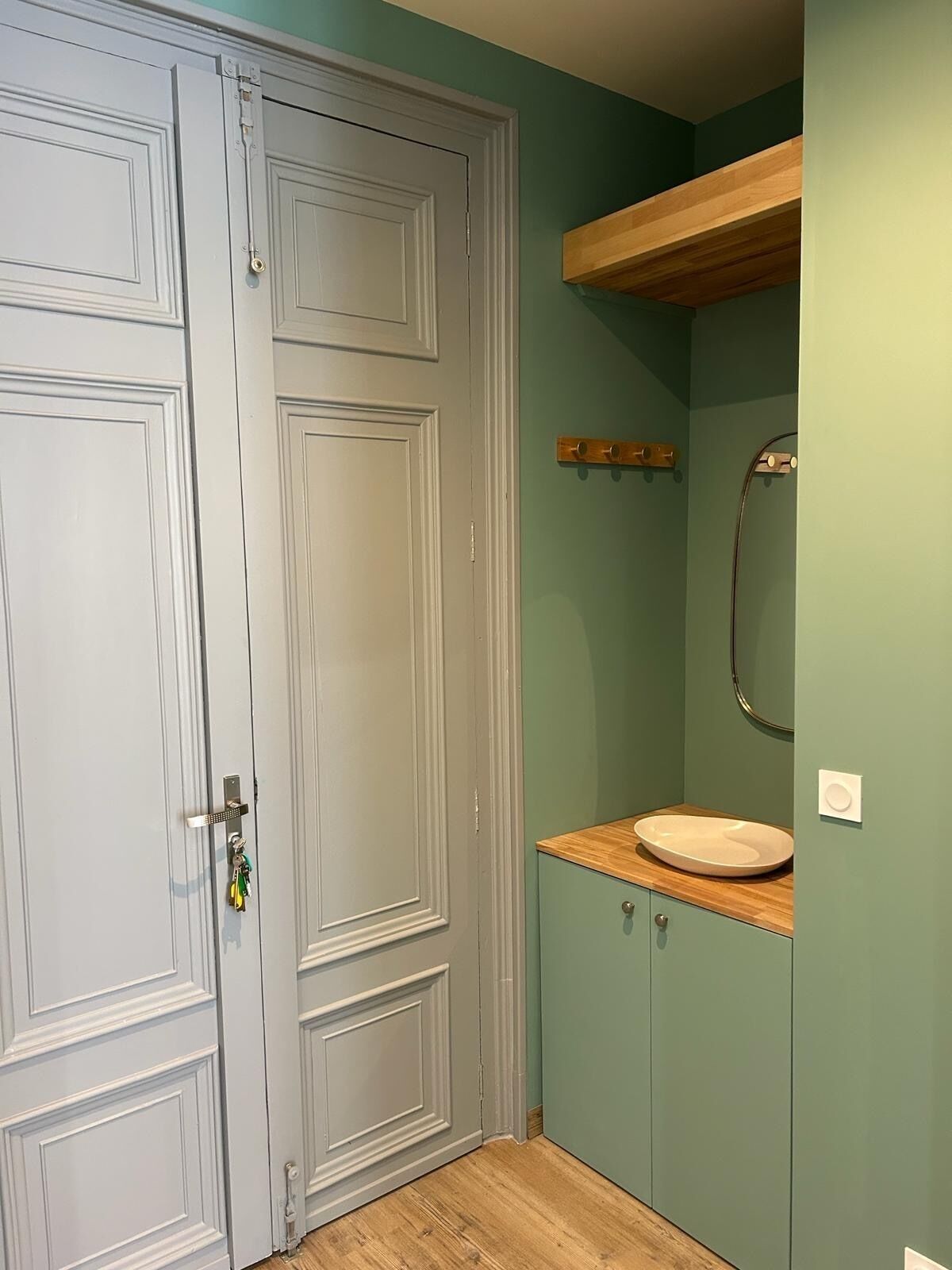 Een badkamer met een houten wastafelmeubel, een ronde spiegel en een witte wasbak.