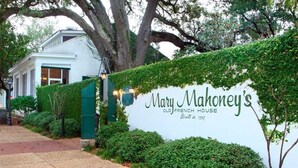 Placa para a Mary Mahoney's Old French House, construída em 1737, com um edifício branco e folhagem verde ao fundo.