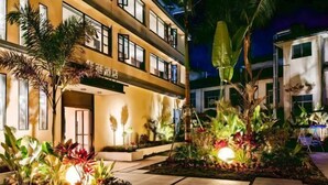 A hotel with a well-lit entrance, a garden with various plants, and a pathway leading to the entrance. - Mohan Huating Hotel (Mengla)