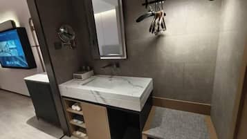 Un baño moderno con un lavabo de mármol, un espejo, un perchero para toallas y un televisor montado en la pared.