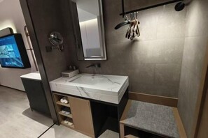 Un bany modern amb un lavabo de marbre, un mirall, un penjador de tovalloles i un televisió penjada a la paret.