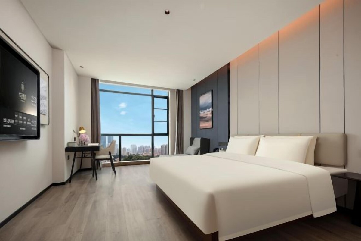 A modern hotel room with a large bed, a desk, a television, and a city view.