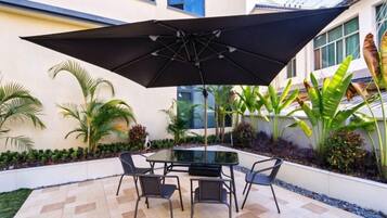 Un patio al aire libre con una mesa, sillas, un gran paraguas y una planta en maceta.