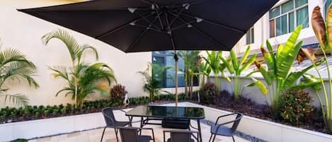 Une terrasse extérieure avec une table et des chaises, un grand parasol et une plante en pot.