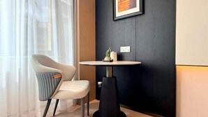 A modern room with a round table, a chair, a framed picture on the wall, and a window with sheer curtains. - Mohan Huating Hotel (Mengla)