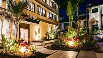 Un hotel con una estructura de varios pisos, iluminación exterior y jardines ajardinados.