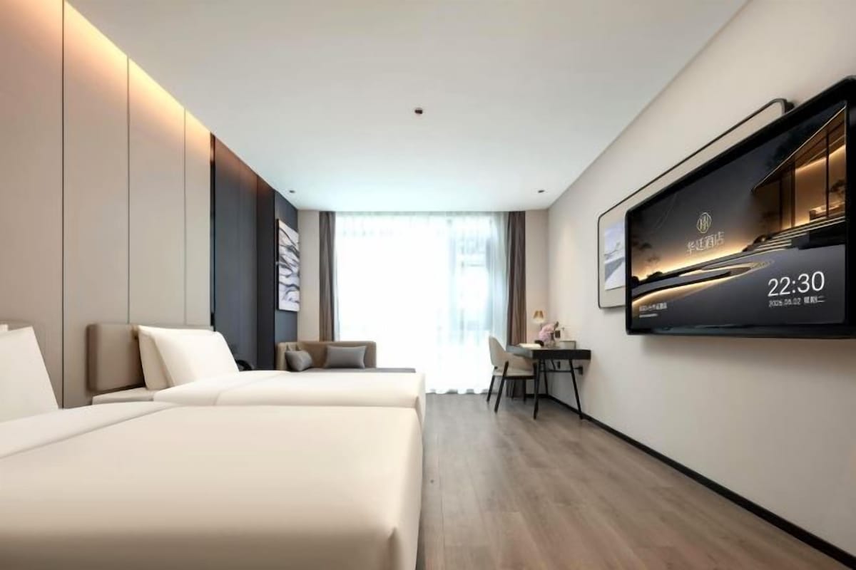 A hotel room with two beds, a desk, and a large TV on the wall.