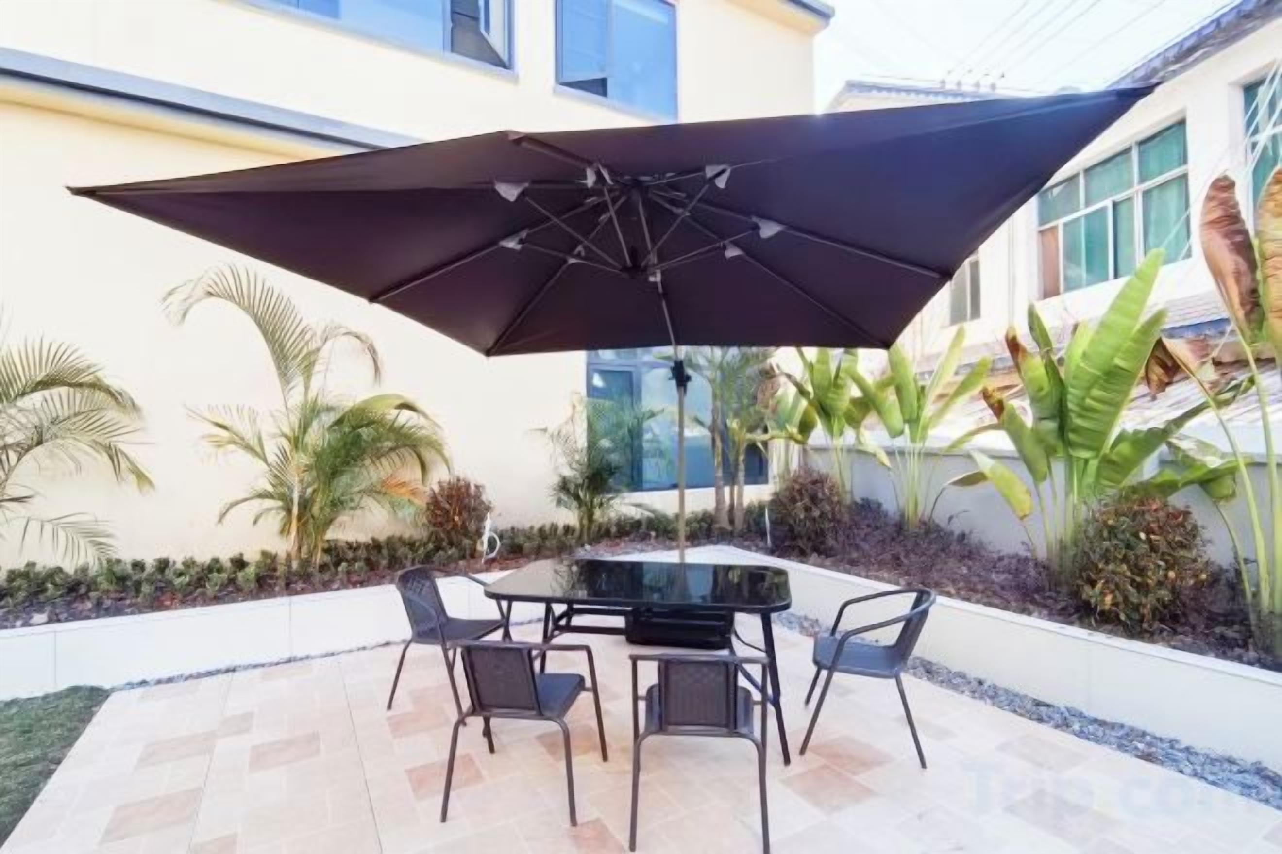 Un patio al aire libre con mesa y sillas, rodeado de plantas y un edificio.