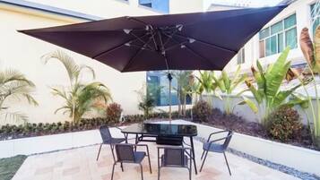 Un patio al aire libre con mesa y sillas, rodeado de plantas y un edificio.