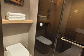 Un bany modern amb una cabina de dutxa de vidre, un vàter i una estant amb tovalloles netejades.