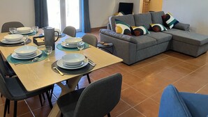A dining area with a table set for four, a grey sofa with colorful cushions, and a window with curtains. - Relax, swim and unwind at this Portuguese house 5 minutes from Sertã, Portugal. (Sertã)