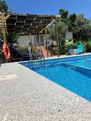 A swimming pool with a tiled edge, a wooden pergola overhead, and a lifebuoy on the left.