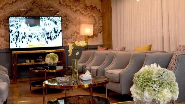 A modern living room with a flat-screen TV, leather sofas, a coffee table, and decorative flowers.