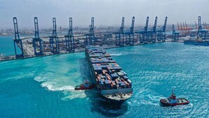A large cargo ship docked at a port with multiple cranes and a tugboat nearby.