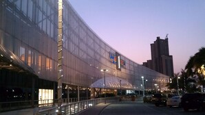 A large, modern building with a curved glass facade, a prominent sign with the number 1, and a tall adjacent building in the background.