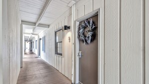 A corridor with wooden floors and white walls, a door with a number plaque, and a wreath on the wall.