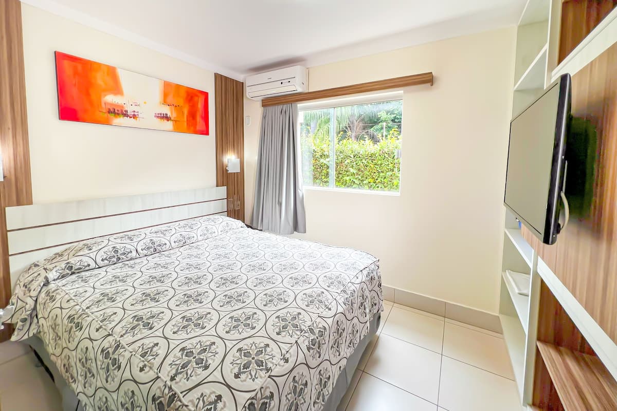 Une chambre moderne dotée d’un grand lit, d’un téléviseur à écran plat, d’un appareil de climatisation et d’une fenêtre avec des rideaux.