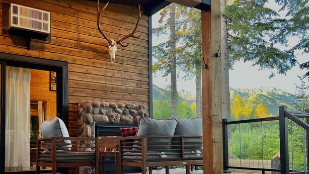 Une cabane en bois dotée d’un bain à remous, d’une cheminée en pierre et d’un espace extérieur aménagé avec une vue sur les arbres et les collines.