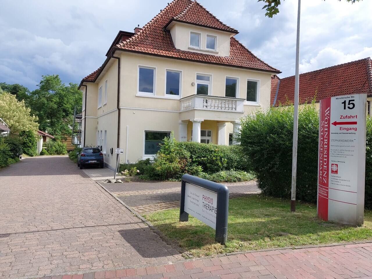 A two-story building with a red-tiled roof, a sign indicating it is a residential property, and a sign for a physiotherapy clinic.