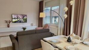 Una sala de estar moderna con un sofá, una mesa de comedor lista para cuatro personas y un televisor montado en la pared.
