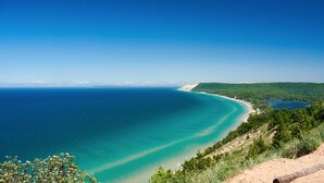 Eine Küstenlandschaft mit klarem Blick auf das Meer, einem Sandstrand und einer bewaldeten Hügelskette.