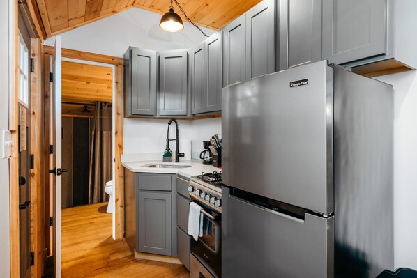Una cocina moderna con armarios grises, un refrigerador de acero inoxidable y techo de madera.