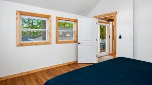 Ein Schlafzimmer mit einem Bett, zwei Fenstern und einer Tür, die zu einem Außenbereich führt.