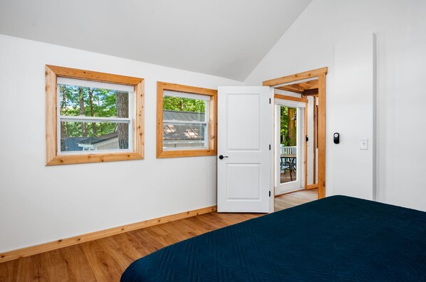 Un dormitorio con una cama, dos ventanas y una puerta que da a un espacio exterior.