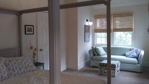Een slaapkamer met een hemelbed, een bank, een klein tafeltje en een raam met zonwering.