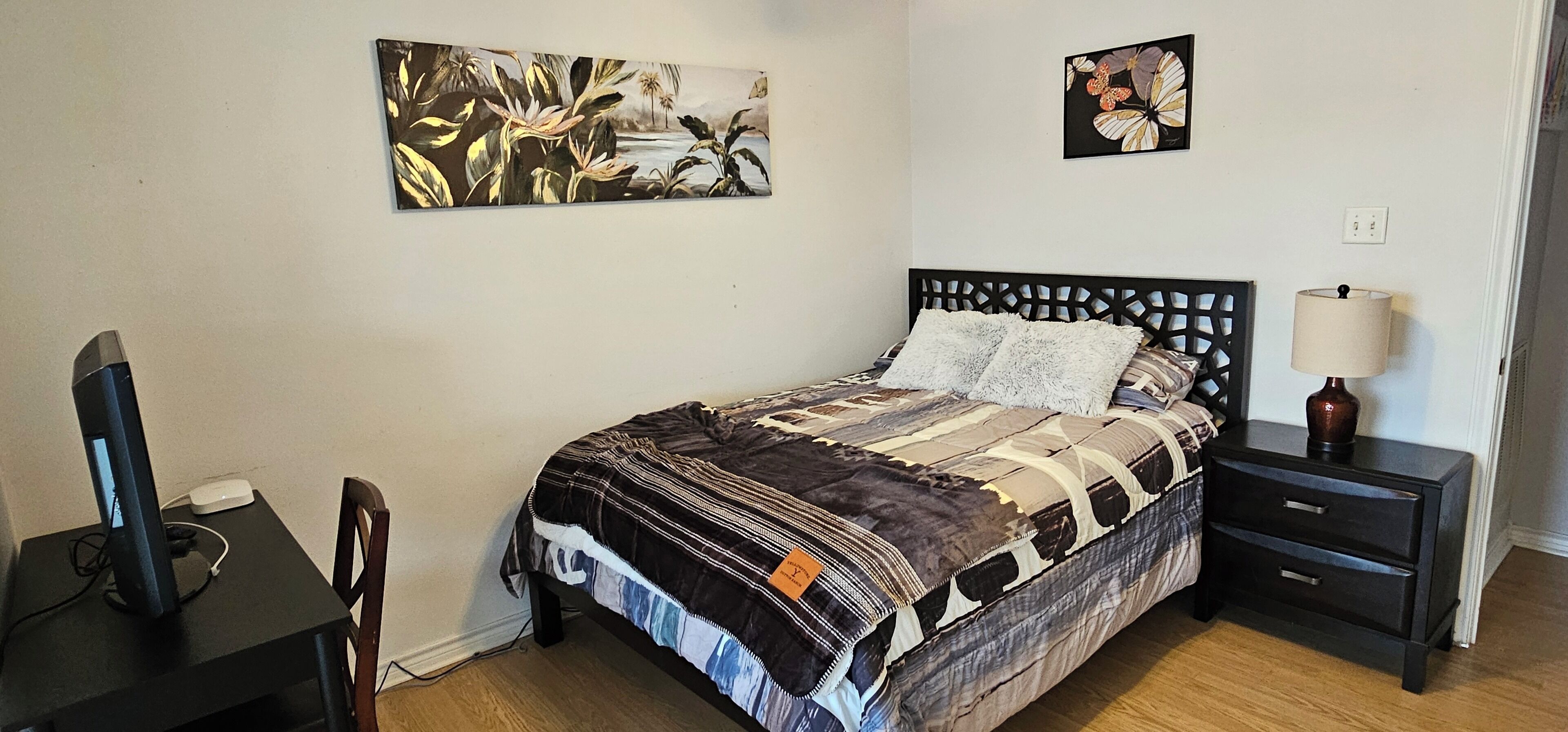Ein Schlafzimmer mit Bett, Schreibtisch, Stuhl, Nachttisch und zwei Wandbildern.