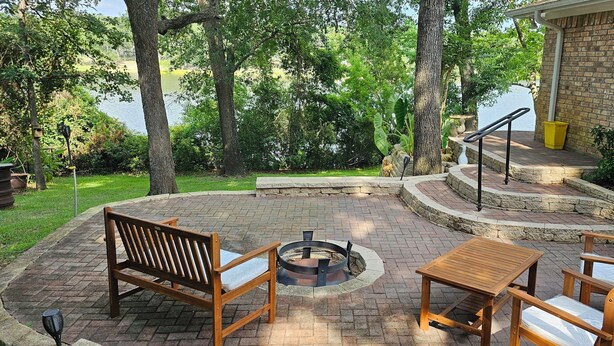 Un patio con un hogar para la chimenea, mobiliario de madera y vista al lago.