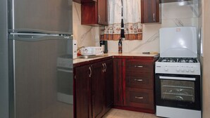 A compact kitchen with a stainless steel refrigerator, wooden cabinets, a gas stove, and a built-in oven.