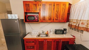 Una cocina compacta con refrigerador, microondas, lavamanos y armarios de madera.