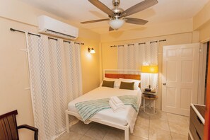 Une chambre à coucher comprenant un lit, un ventilateur de plafond, un appareil de climatisation, une table de chevet avec une lampe et une porte.