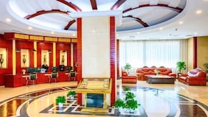 Eine Hotlellobby mit Empfangsschalter, Sitzgelegenheiten und einer zentralen Säule.