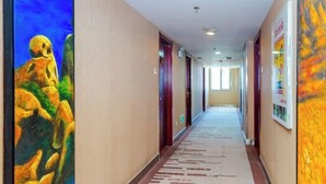 Ein Hotelkorridor mit Teppichmuster, Türen und Kunstwerken an den Wänden.