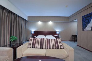 A hotel room with a bed, a sofa, a table, and a painting on the wall. - Xinmei Hotel (Urumqi Hongshan Branch) (Urumqi)